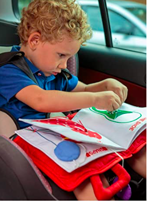Young boy tying a shoe in a quiet book for toddlers while riding in a car. Busy books can be used to keep toddler occupied.